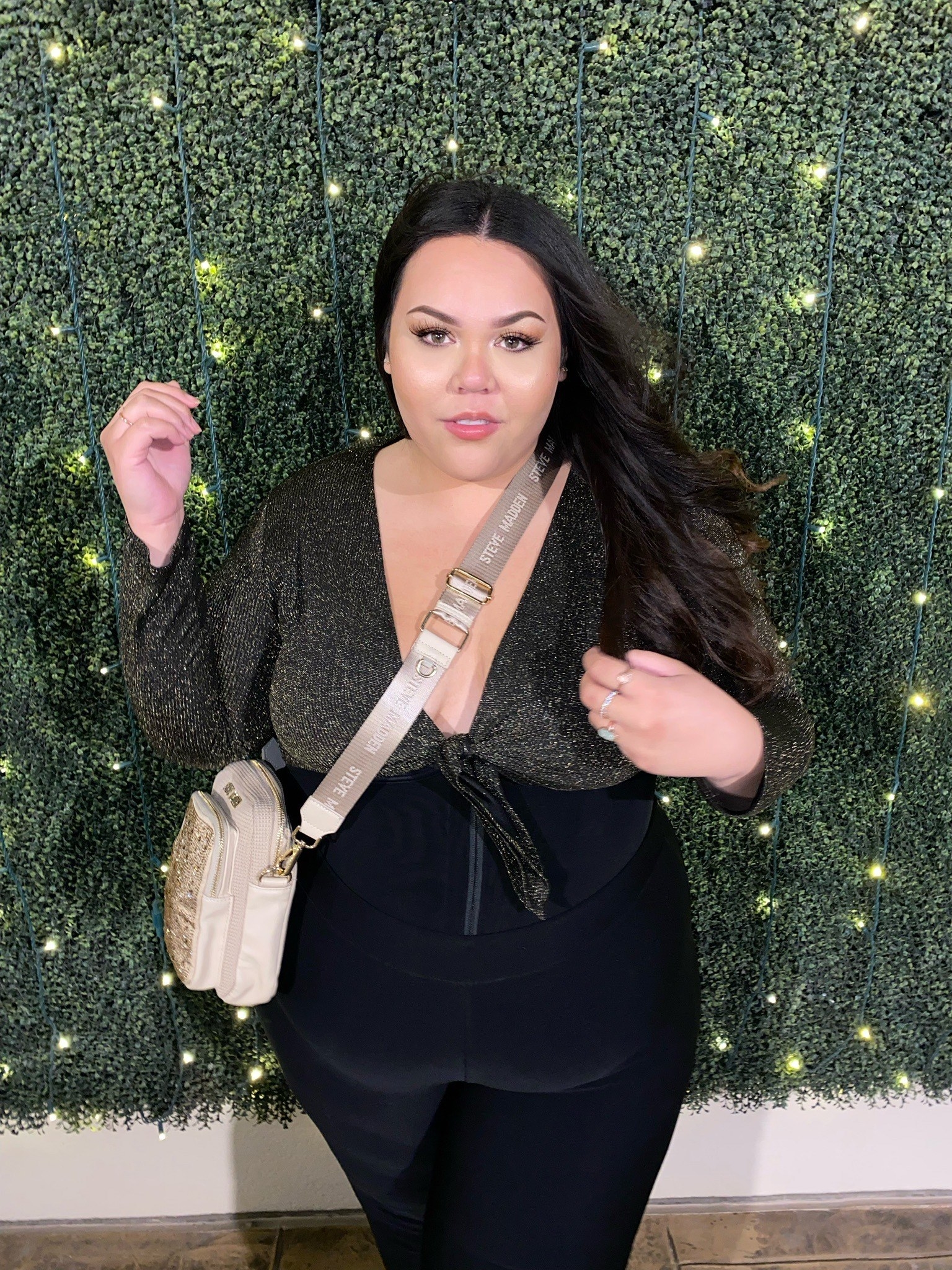 Julia wearing a shoulder bag stands in front of a green lit background