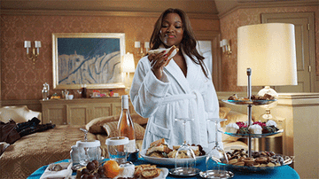 woman eating a sandwich from a lavish room service spread in a hotel room