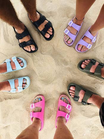 reviewer pic of multiple people wearing the slides in pink, light blue, purple, and dark green colors while they're walking on the beach