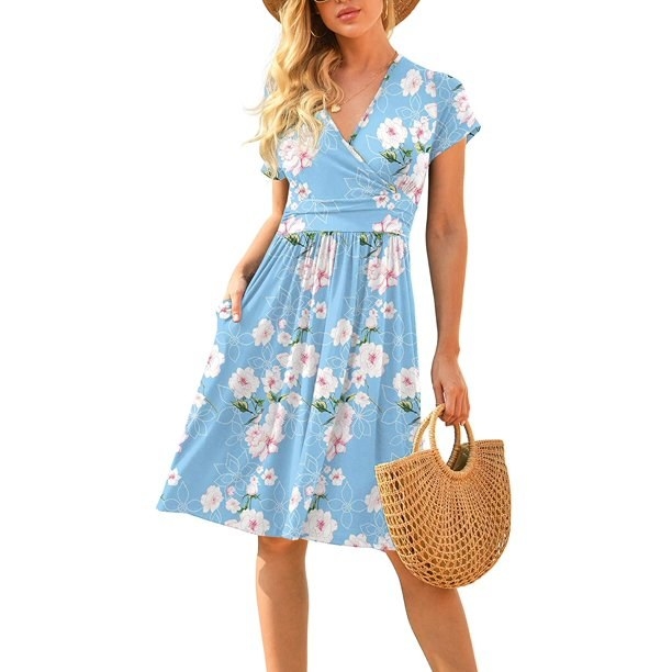 model wearing light blue, floral dress and holding woven handbag