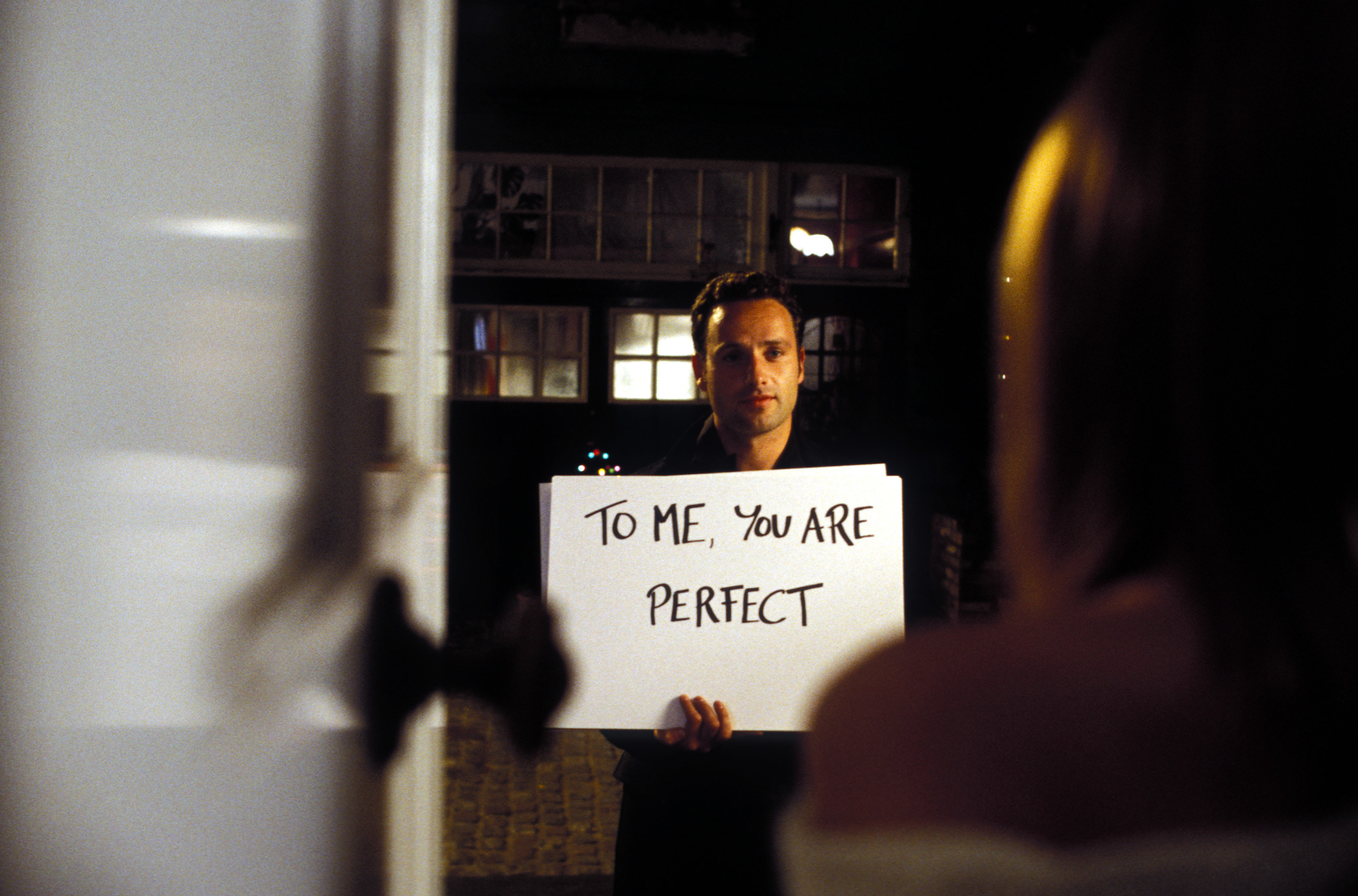 A man holding a sign to a woman saying, &quot;To me, you are perfect&quot;