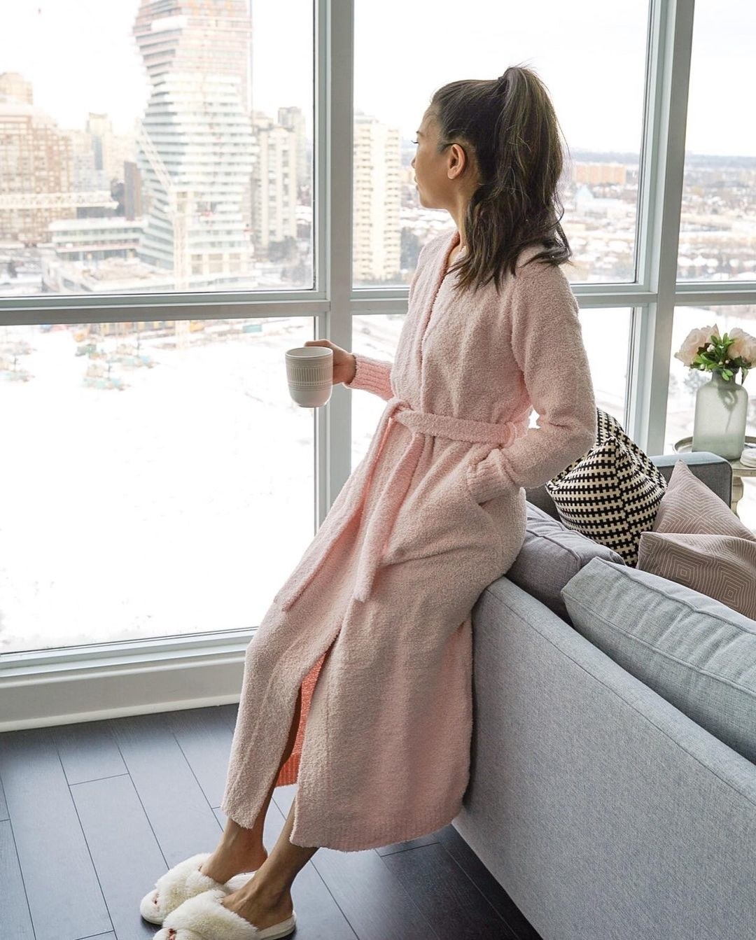 Person wearing the robe and sitting against a couch looking out the window