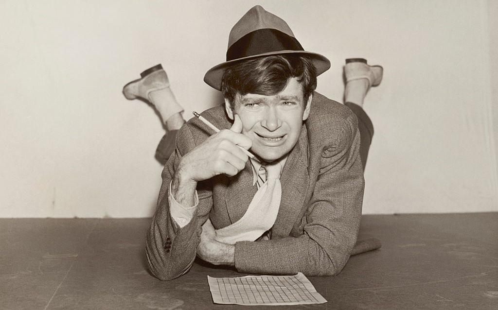 Buddy Ebsen looks stumped as he works on a crossword puzzle lying on the floor