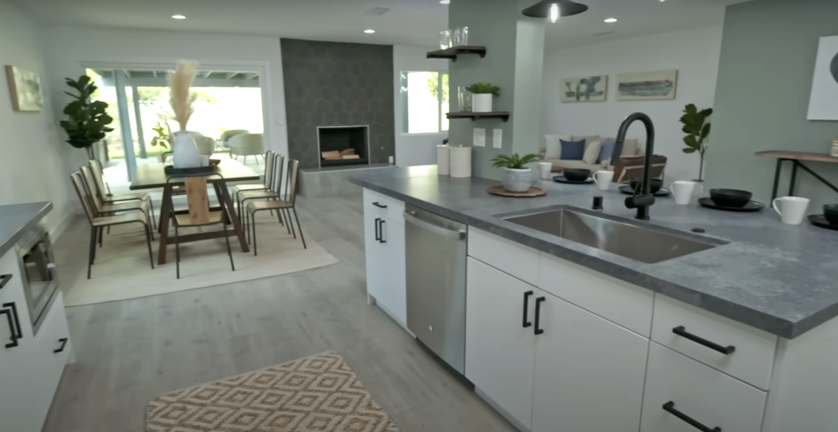 A kitchen and living room designed by Tarek and Christina, including white cabinets with black hardware and grey countertops