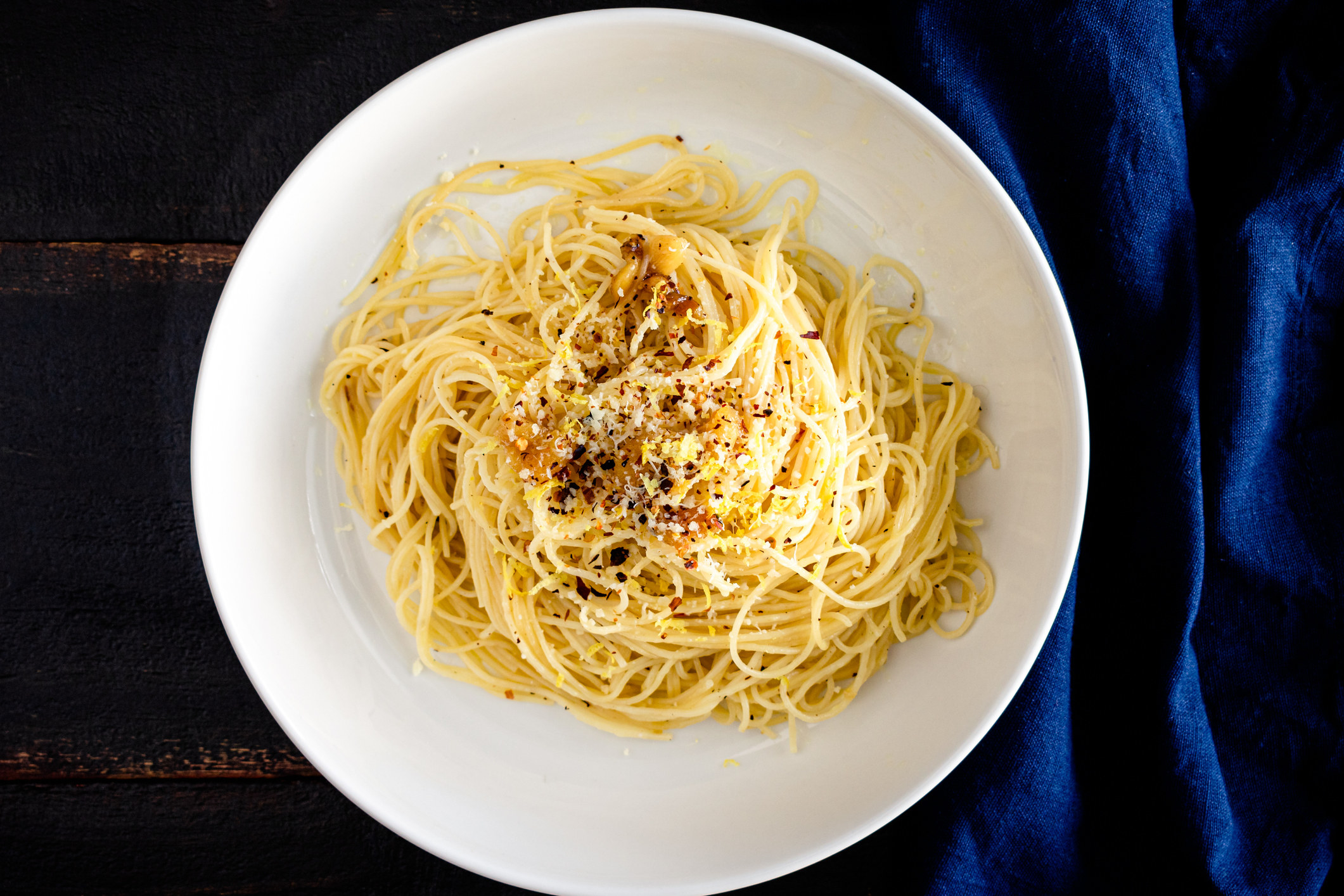 Bowl of pasta topped with red pepper flakes, Parmesan, and lemon zest.