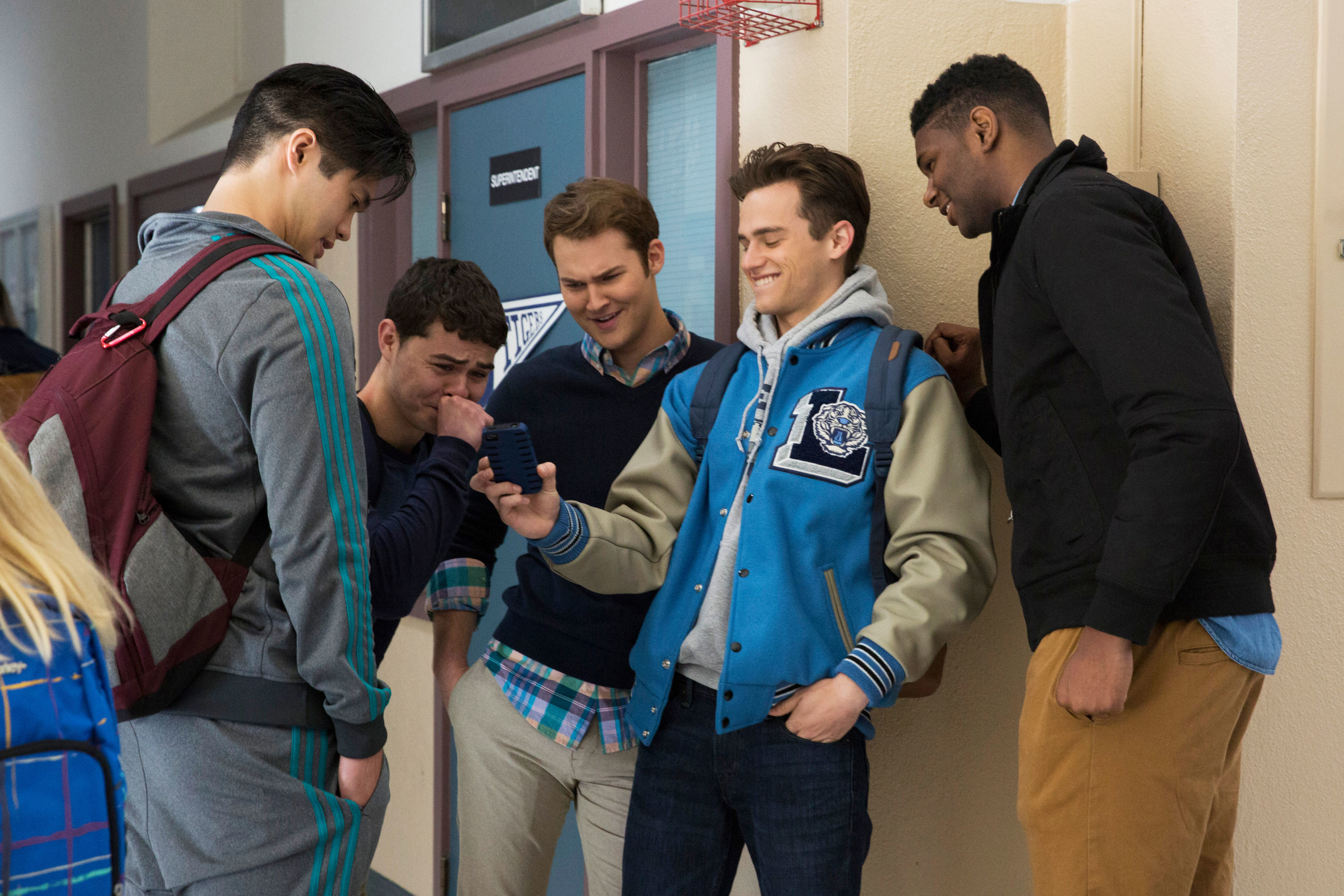 A group of teens looking at a guy&#x27;s phone