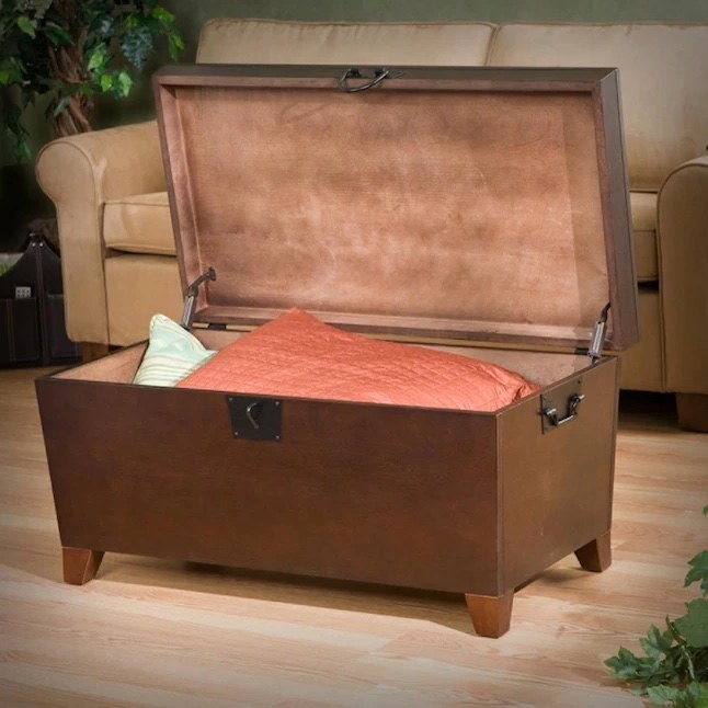 an espresso brown composite wood storage trunk with pillows and a blanket inside