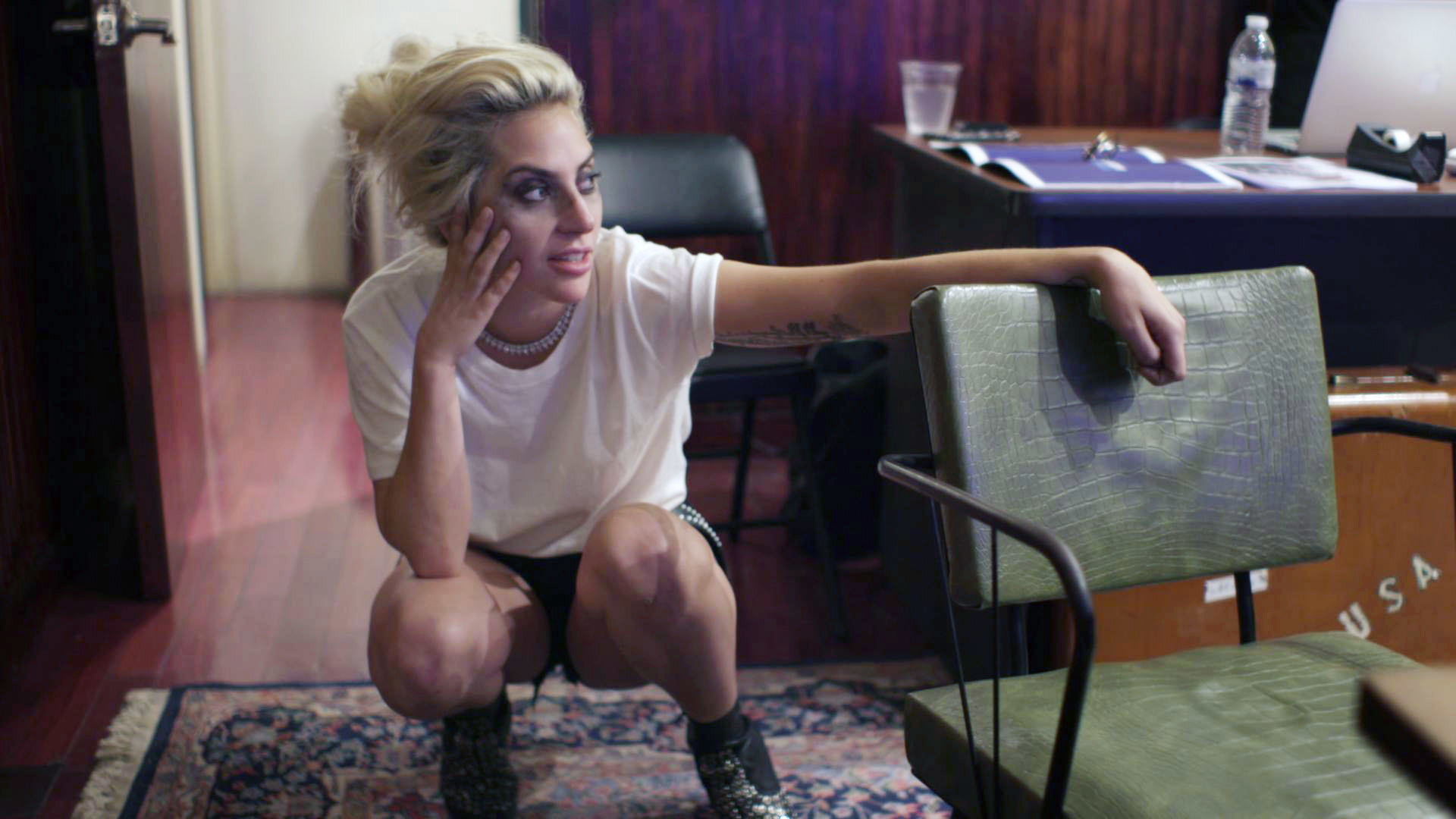 Lady Gaga crouches behind a chair