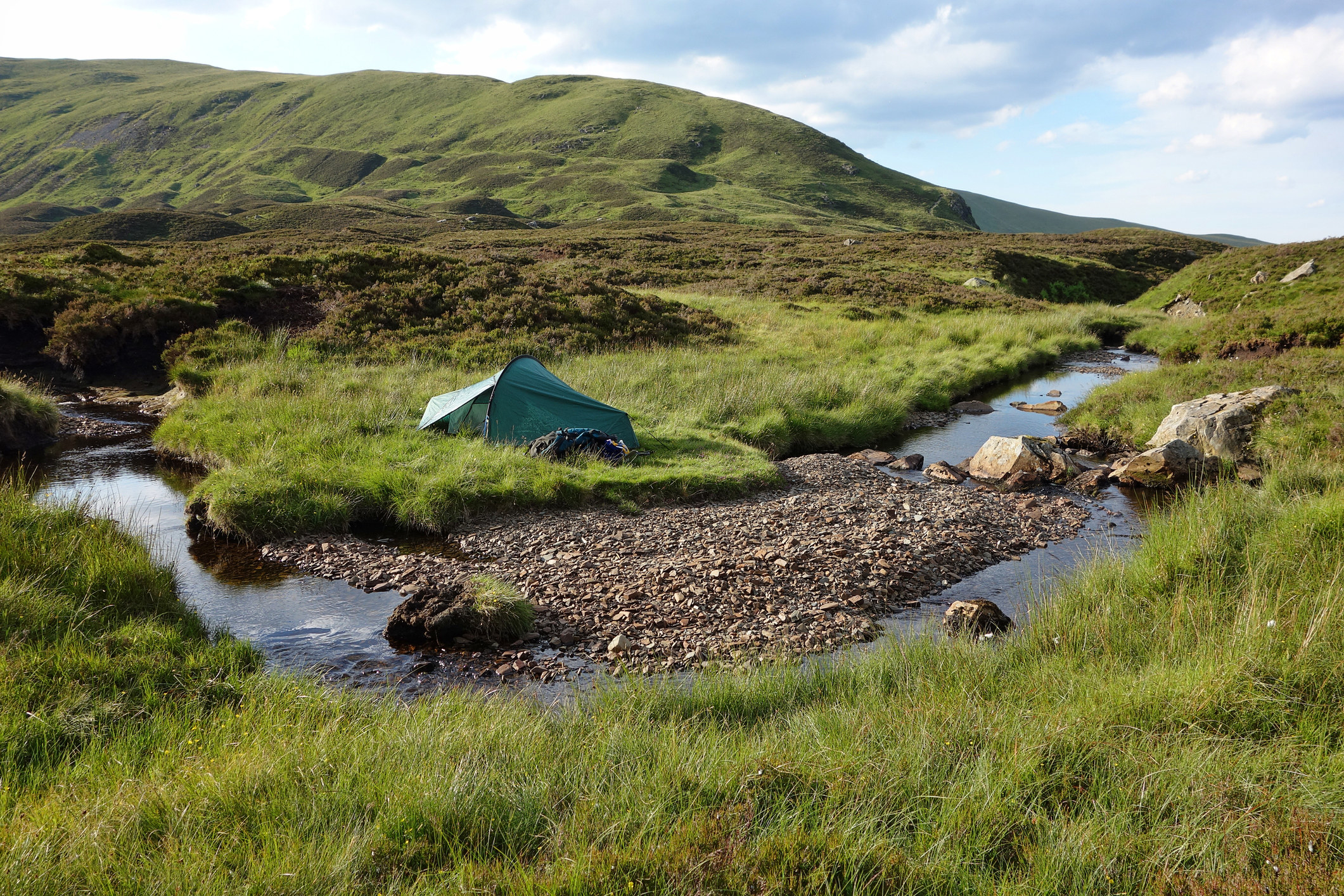 An idyllic wild camping site next to a clear stream.