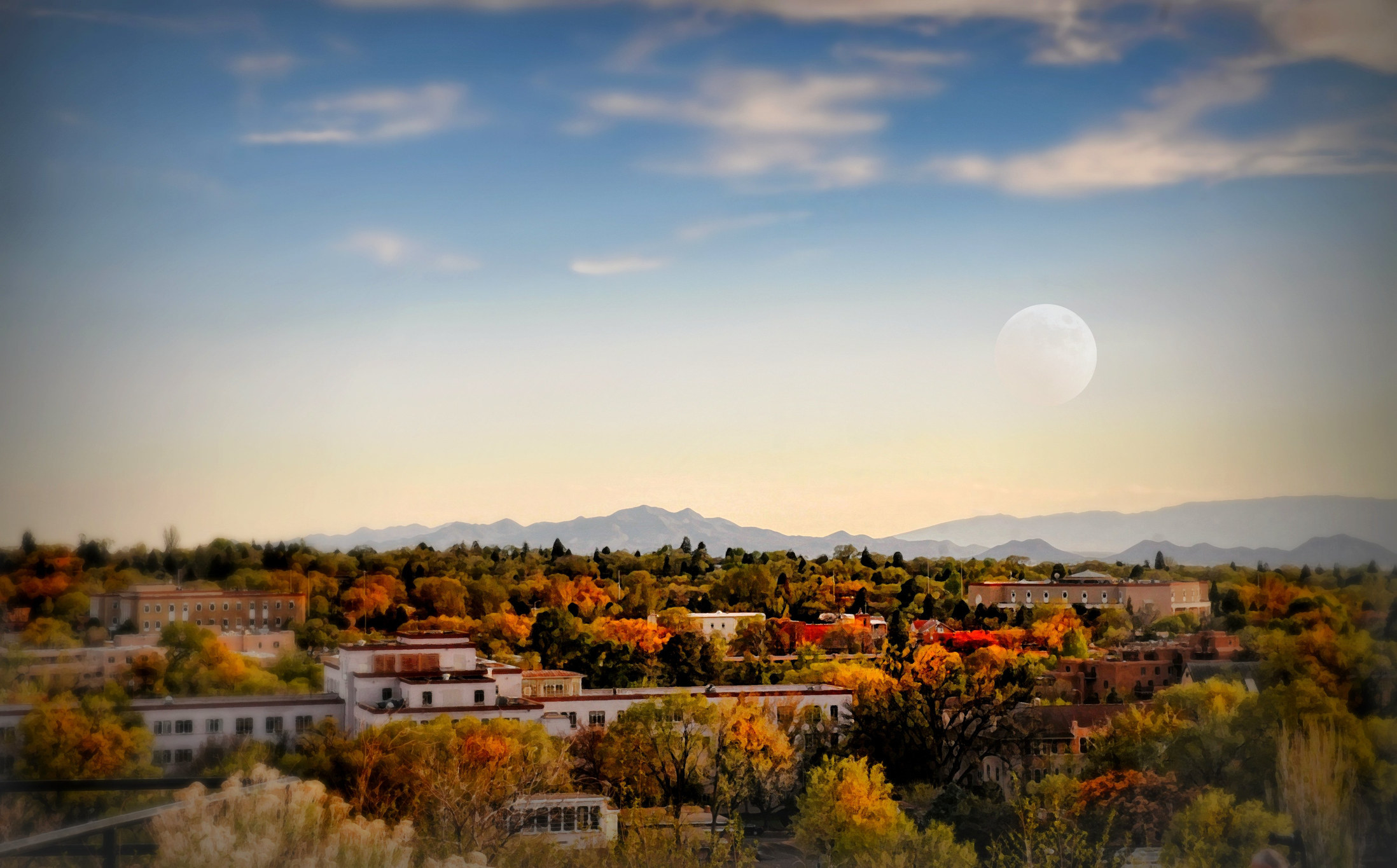 Landscape of Santa Fe New Mexico at dusk with warm colored trees and moon in sky.