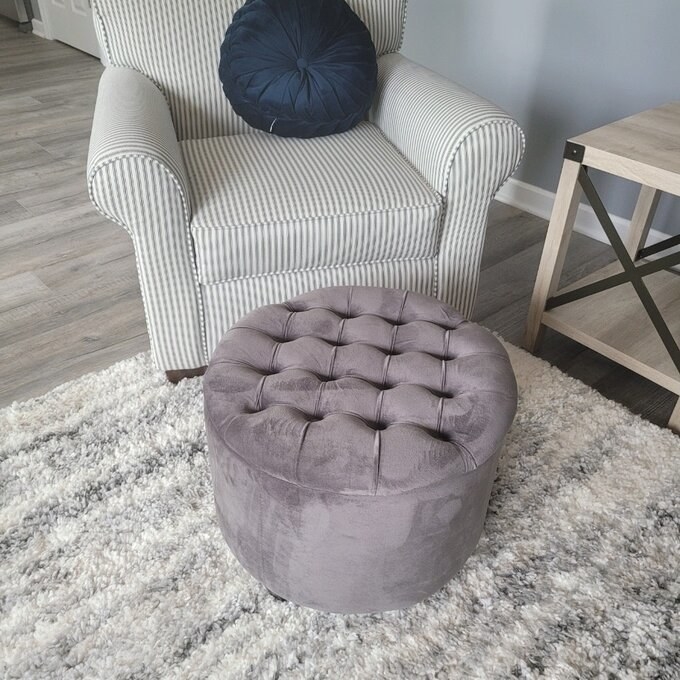 a reviewer photo of the gray ottoman in front of a gray and white striped armchair