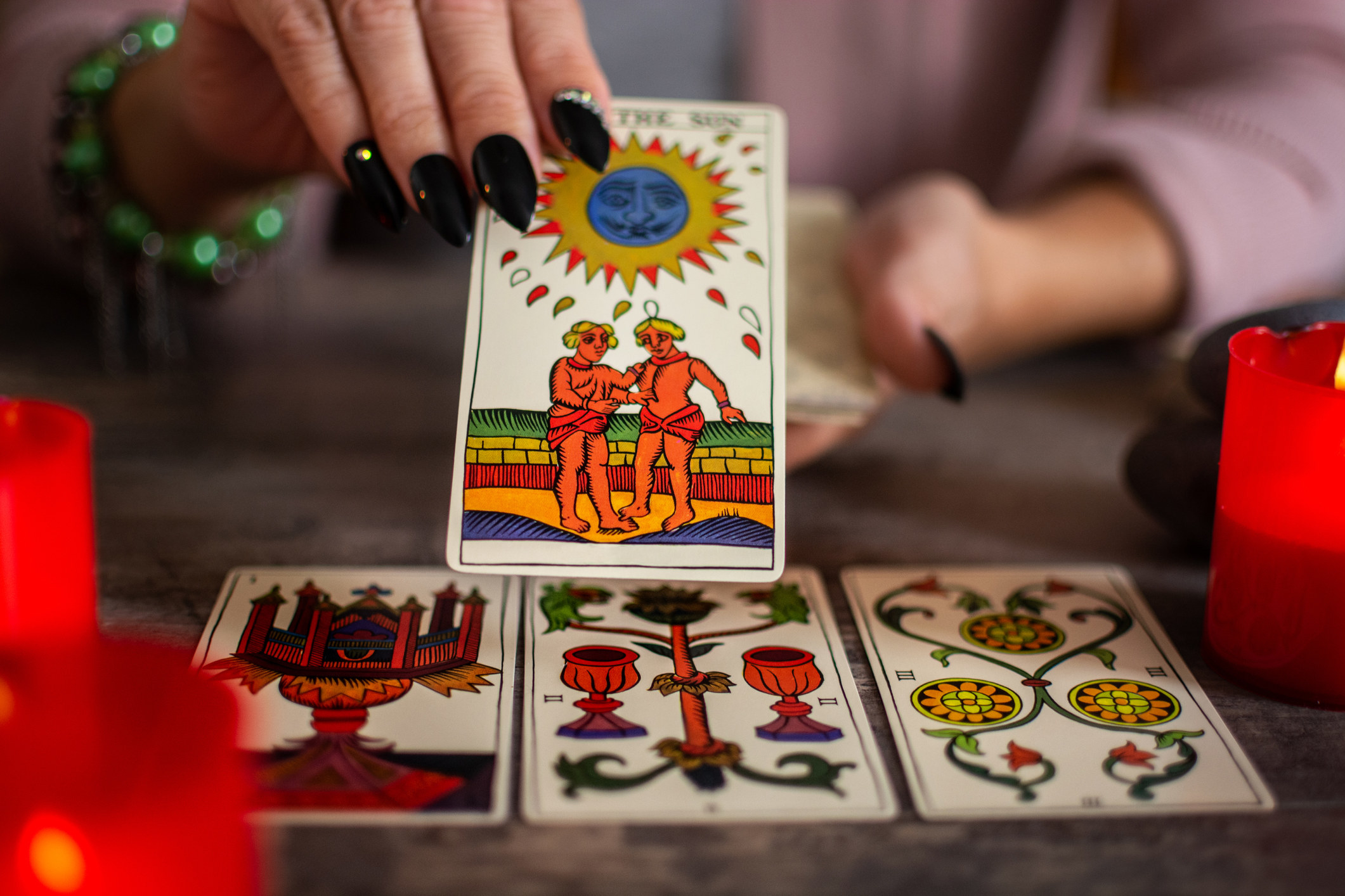 A tarot reader holds a card with two people and the sun