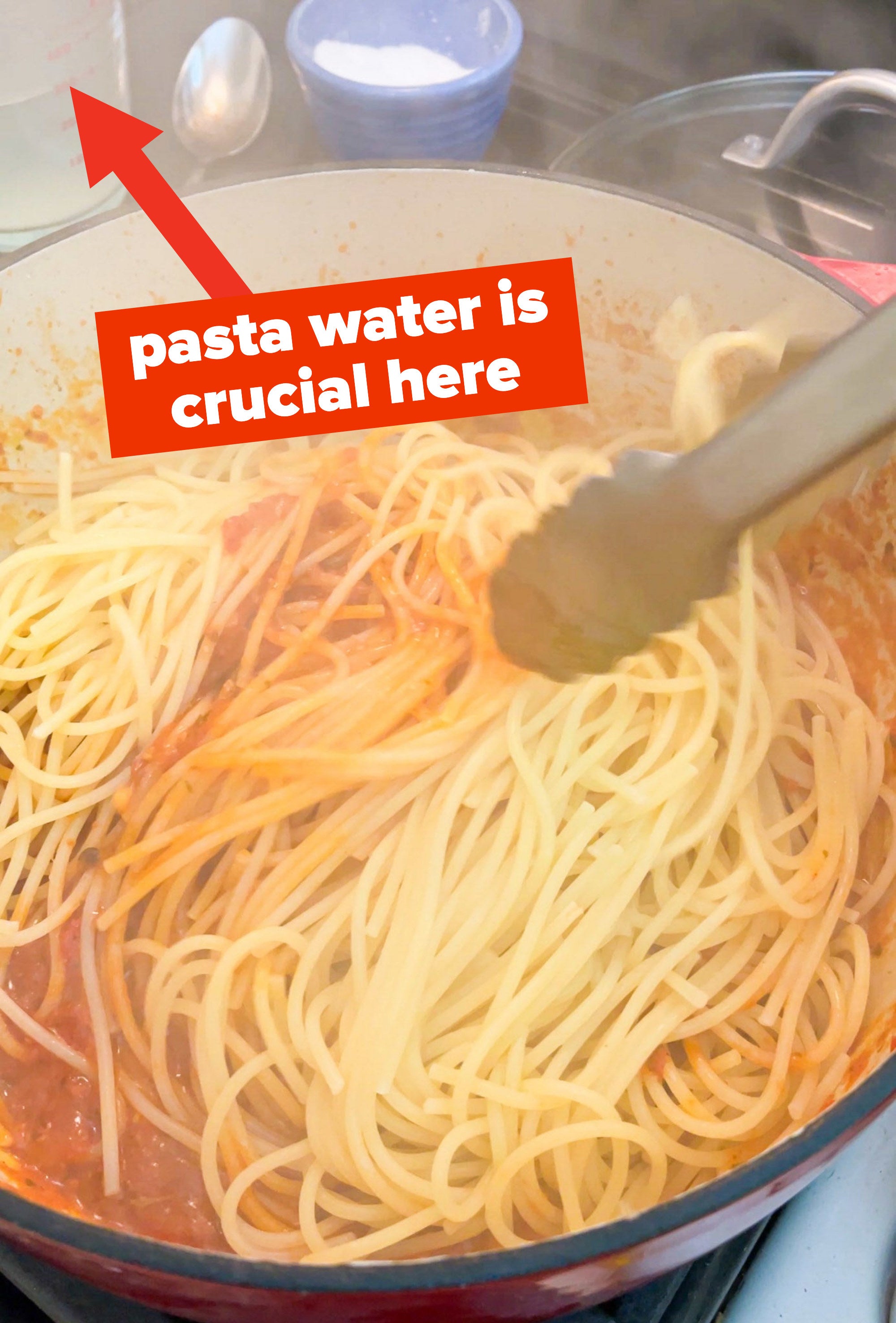 spaghetti being mixed into the pot of sauce