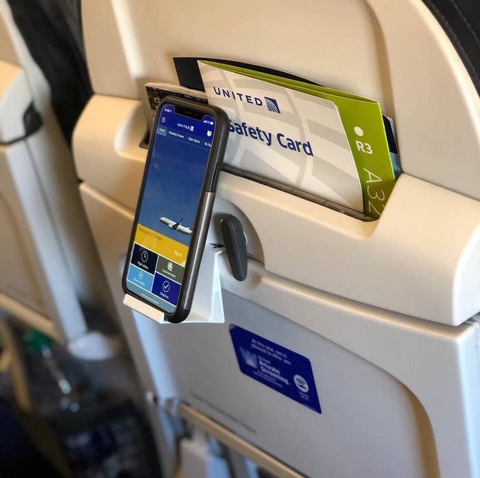 a reviewer photo of the skyclip attached to the tray table with a phone in it
