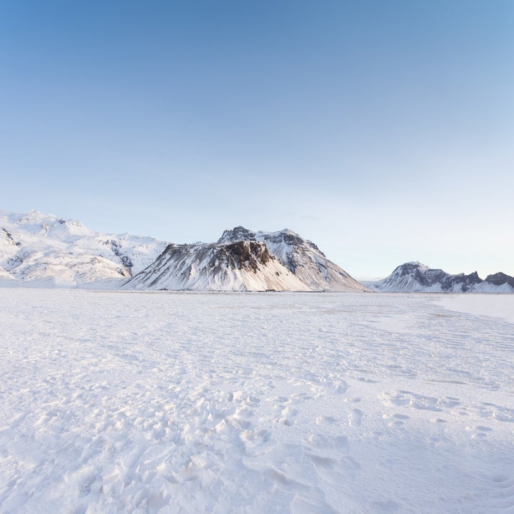 A frozen Icelandic field stretches across Iceland and mountains rise in the distance