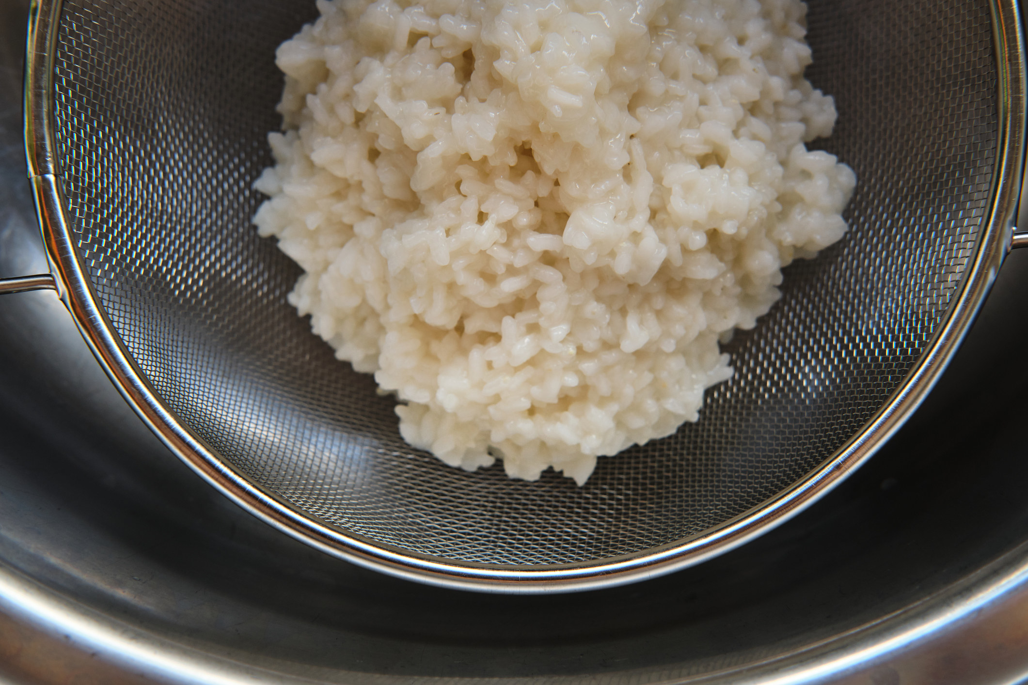 Rice cooked in a grey metal sieve.