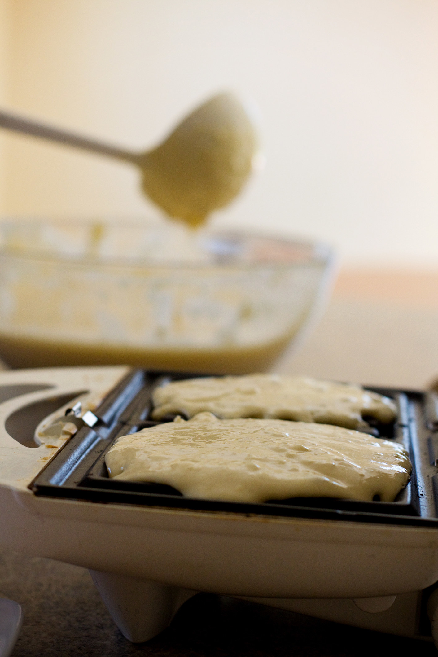A ladle pouring waffle batter into an iron.