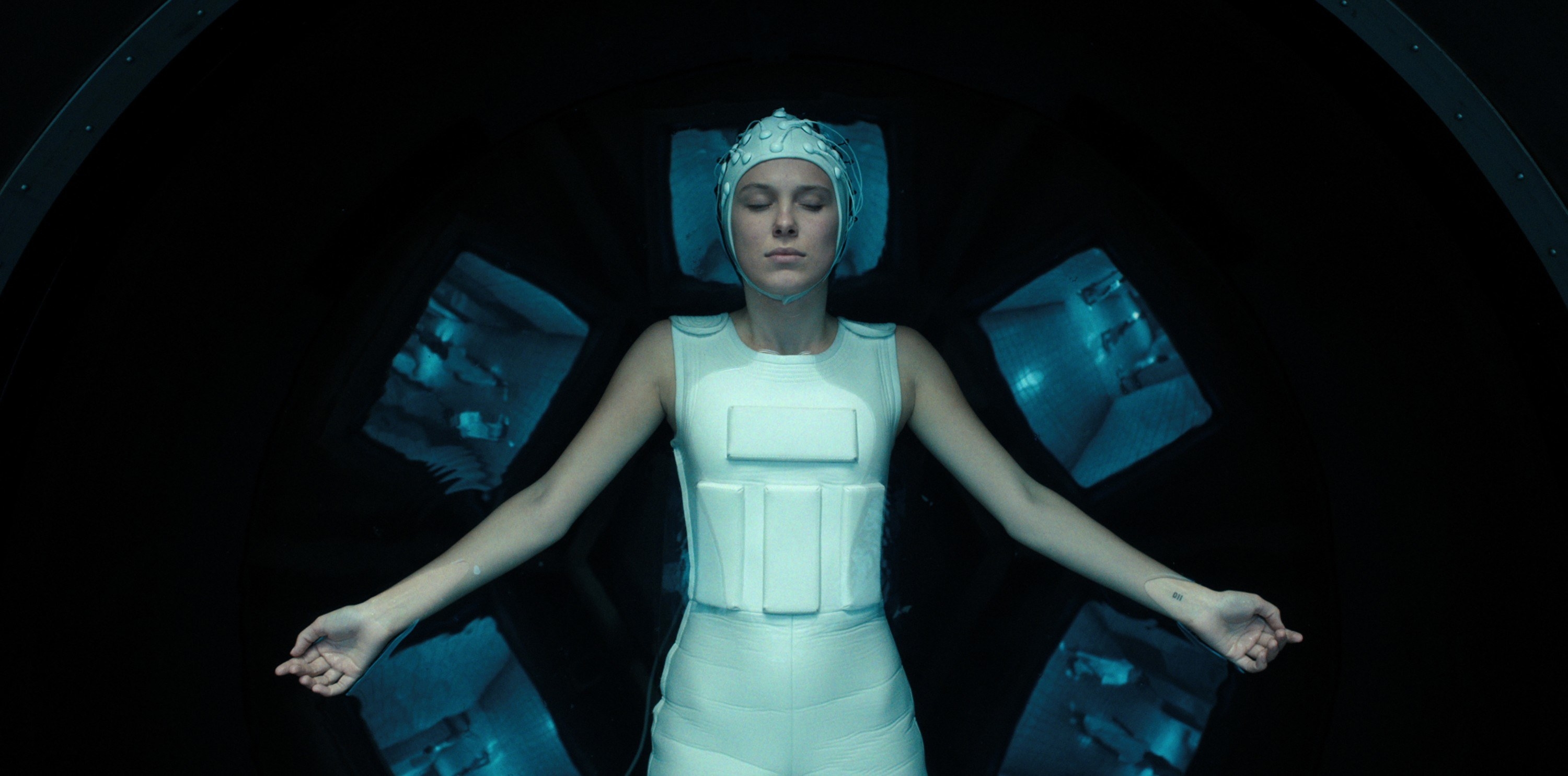 Eleven lies in a water tank in a weighted body suit and matching helmet