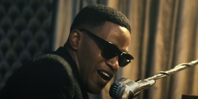 Jamie Foxx as Ray Charles, wearing black sunglasses and singing into an old fashioned microphone