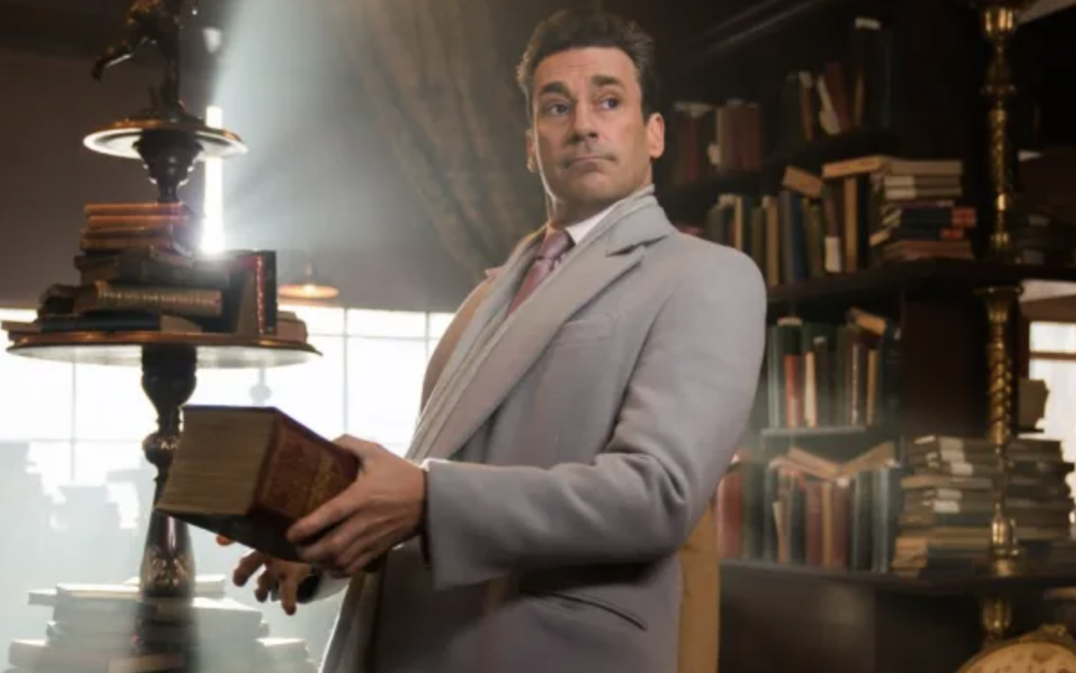 jon hamm's character wears a suit and holds a book