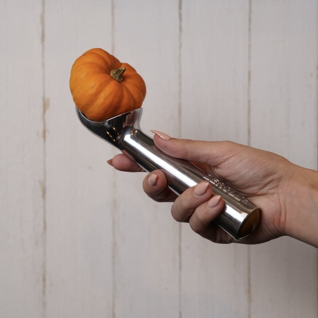 A person holding the ice cream scoop with a pumpkin in it