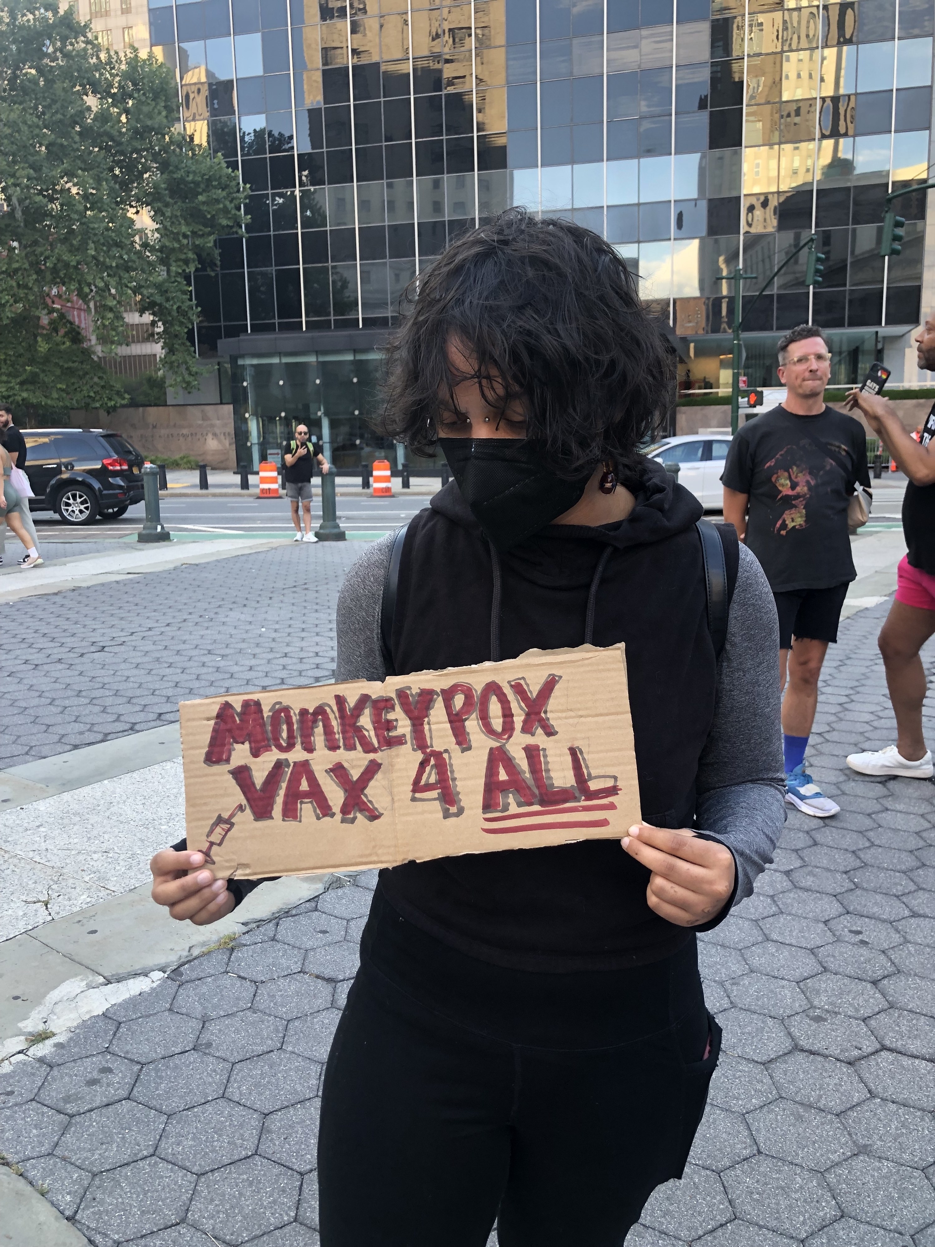Angel holds their protest sign, &quot;Monkeypox vax 4 all.&quot;