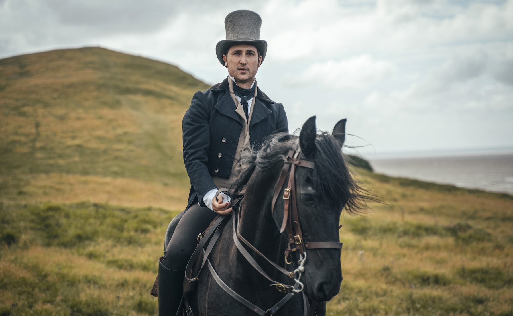 Ben lloyd hughes as alexander colbourne in period costume on a horse in a rugged seaside landscape