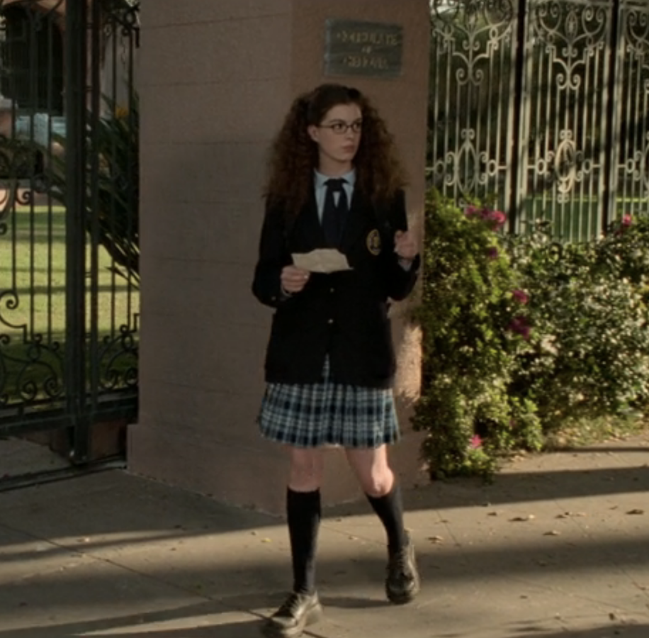 mia in her school uniform of long plaid skirt, long blazer and neck tie