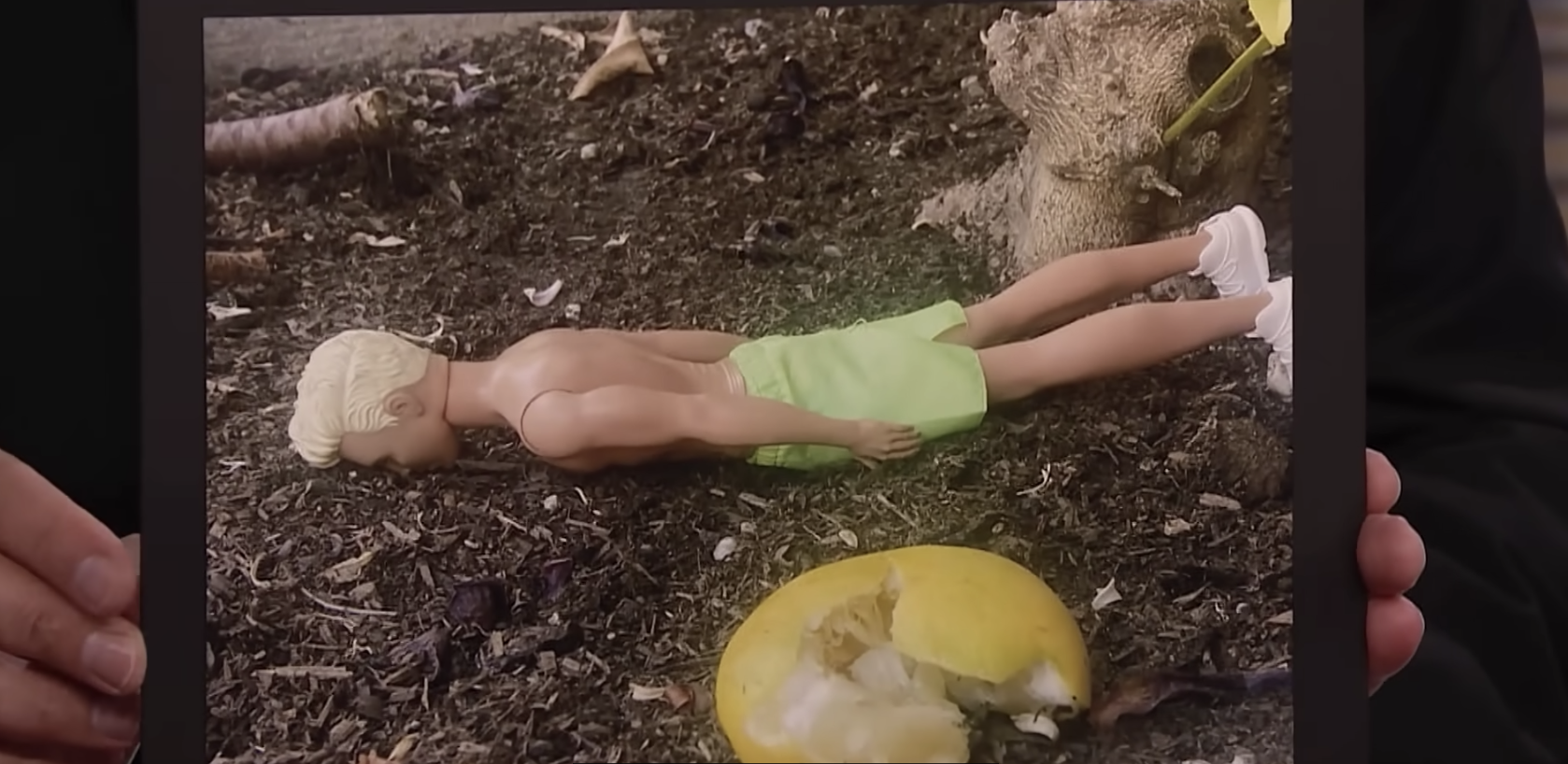 a ken doll face down in the dirt besides the lemon