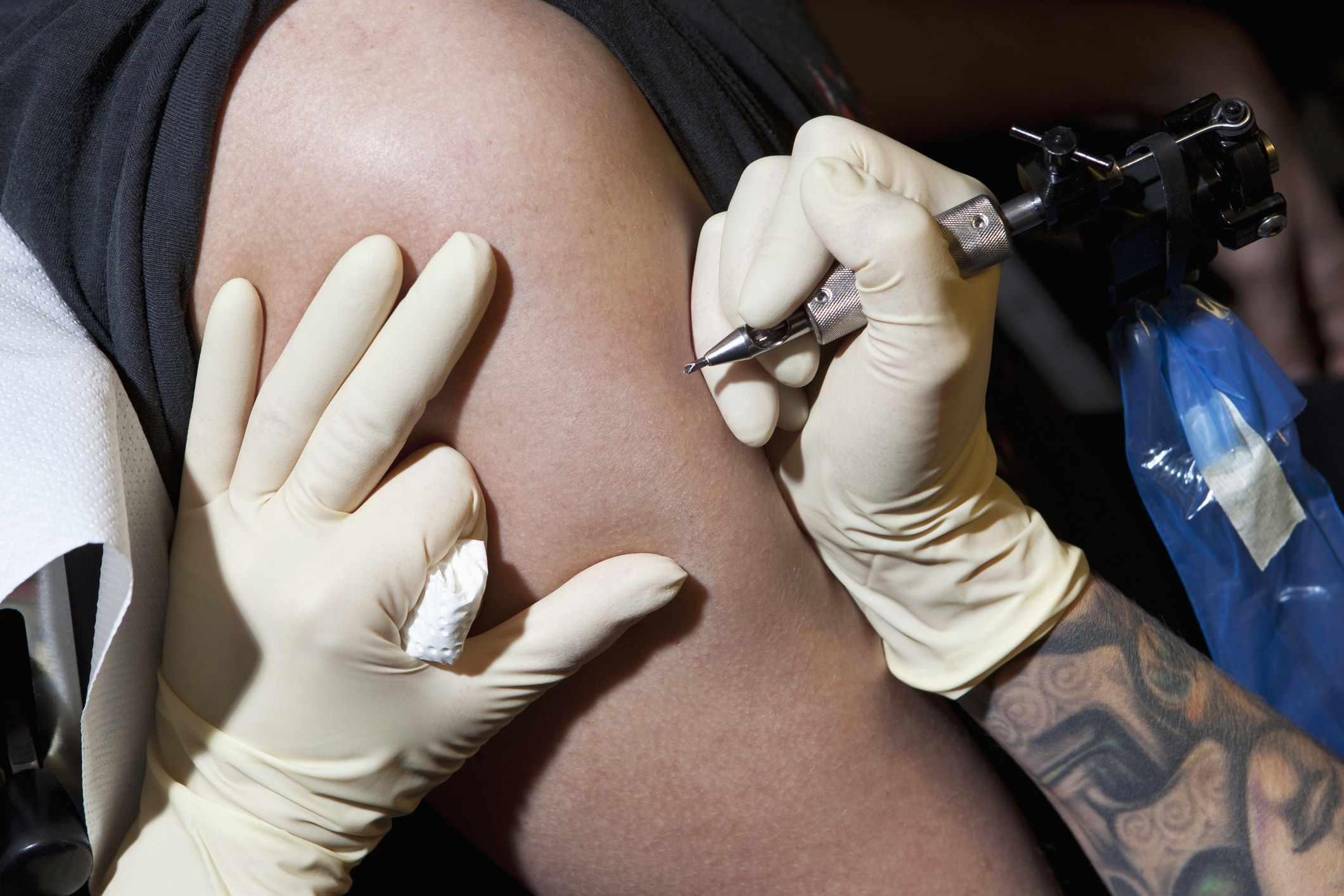 A tattoo artist tattoos an arm