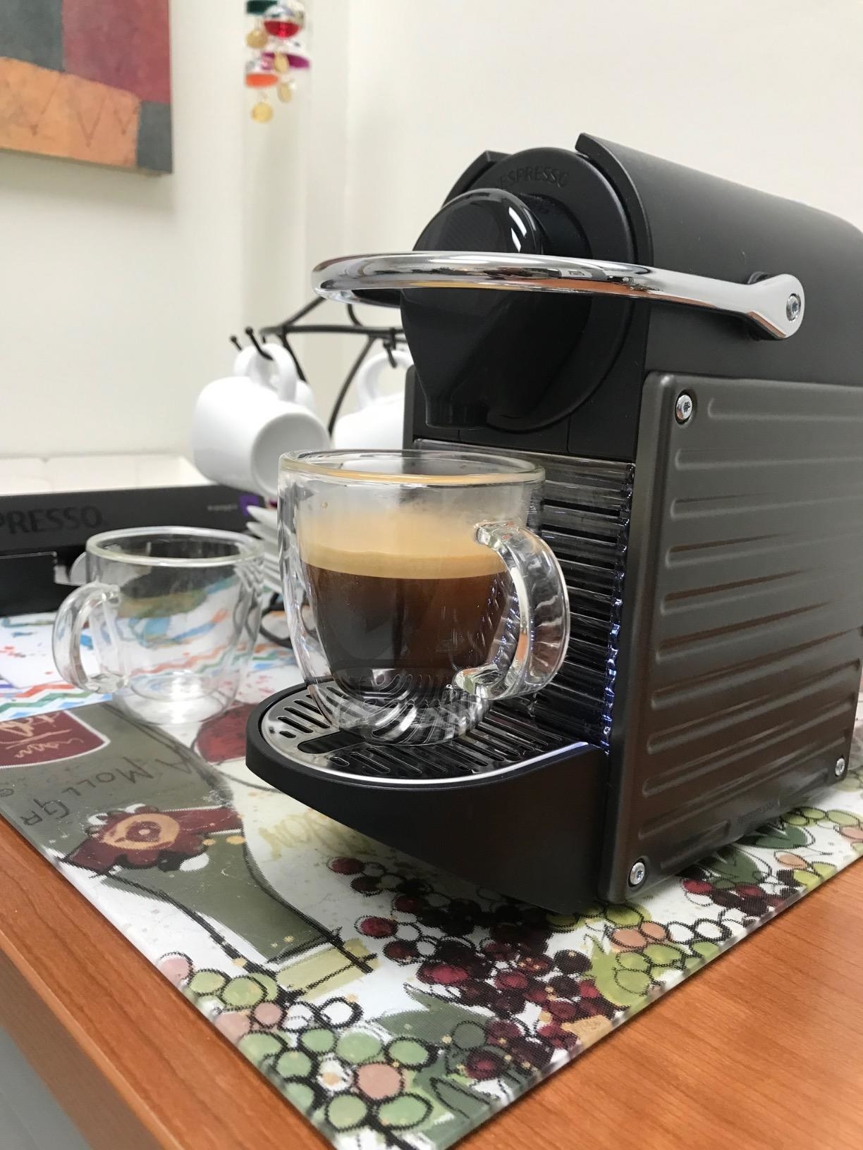 Reviewer&#x27;s photo of the glass mug being filled with espresso from the coffee machine
