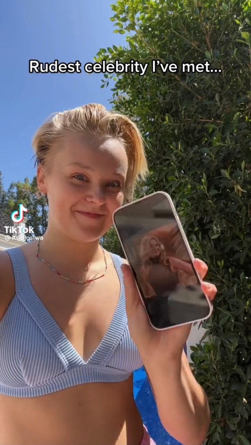 JoJo wears a blue bikini and holds up her phone with a photo of Candace Cameron Bure
