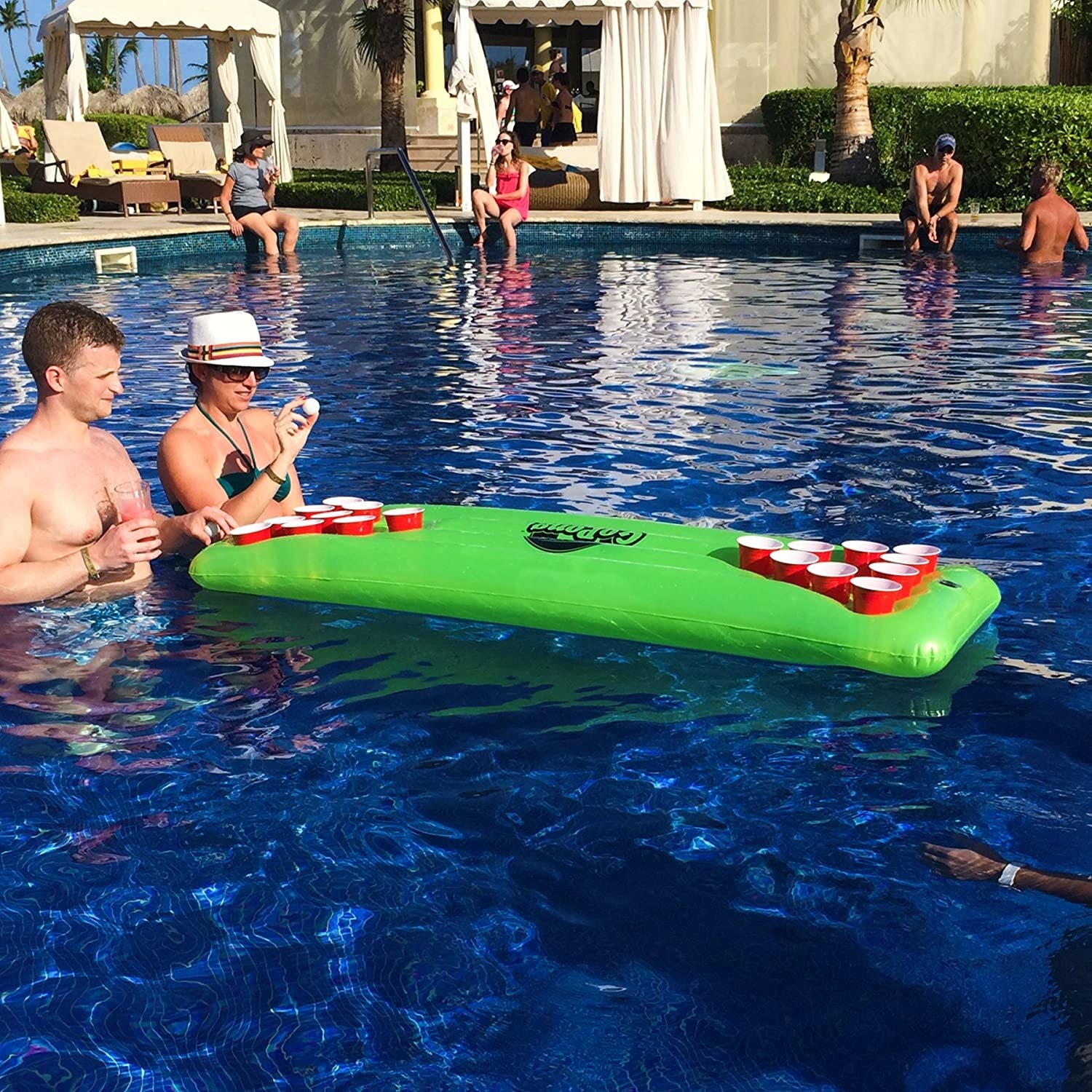 a couple of people playing beer pong at the table in the pool