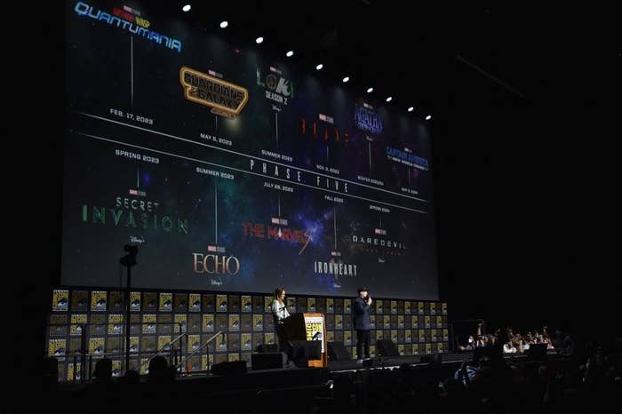 Two people on stage at Comic-Con with the timeline of Marvel&#x27;s Phase Five on a giant screen behind them