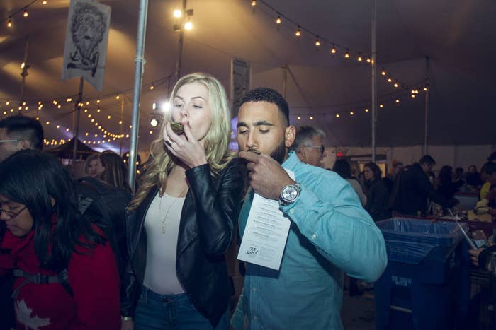 A man and woman slurp oysters in a large tent with string lights