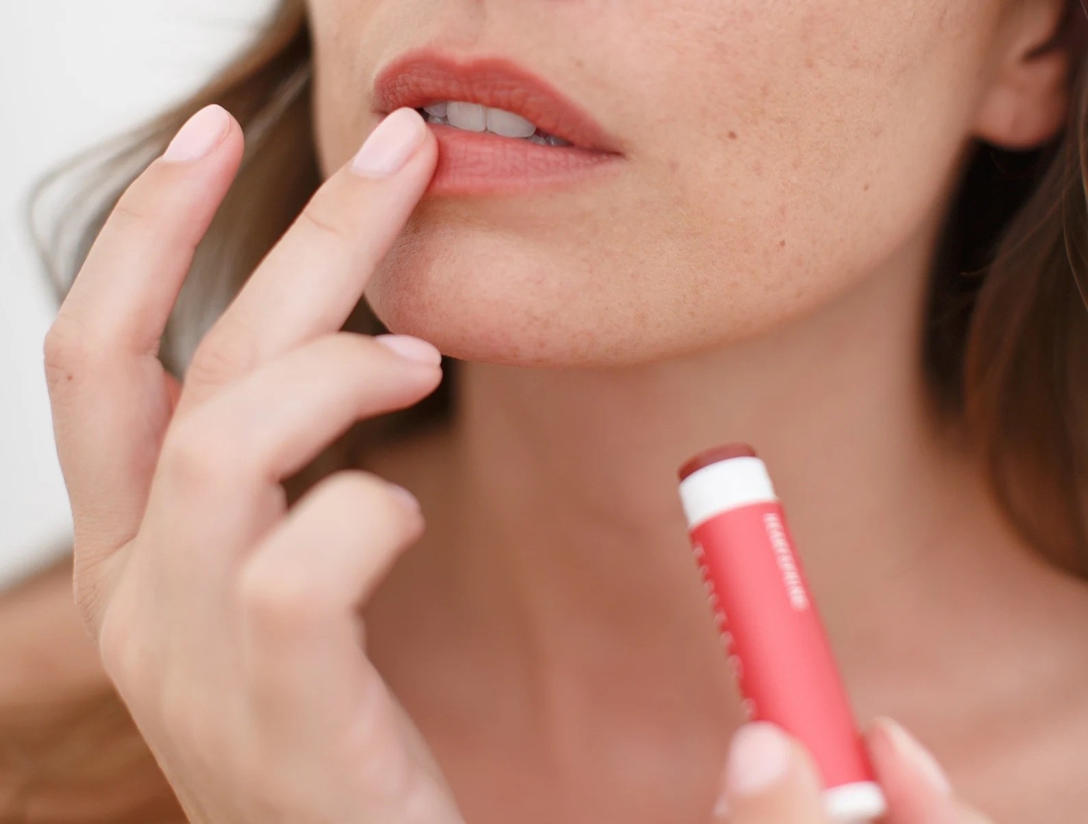 A model applying tinted lip balm to lip from a red tube