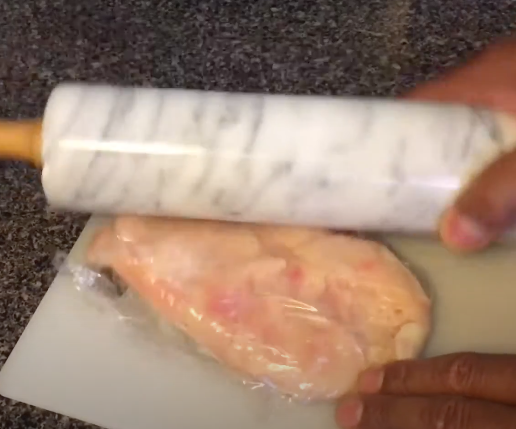 Smashing chicken breast with a marble rolling pin to tenderize it