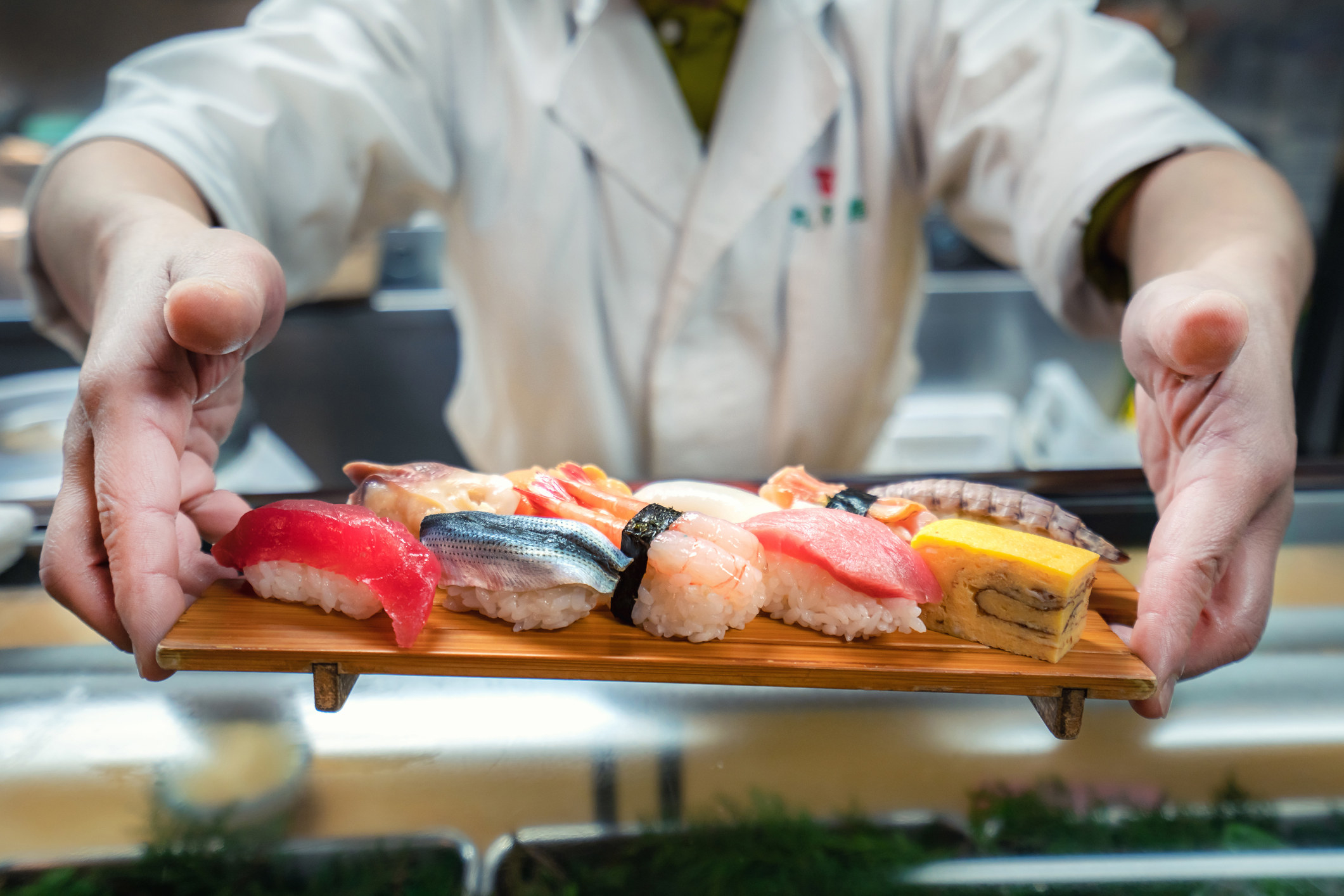 Male chef holding a plate full of sushi at the kitchen.