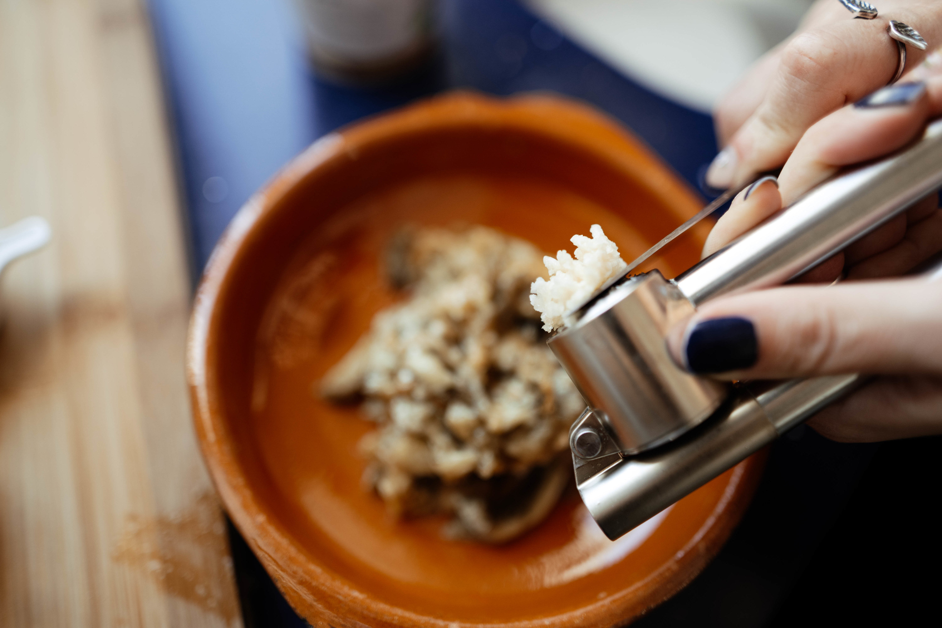 Pressing shallot through garlic press and using knife to put it into bowl