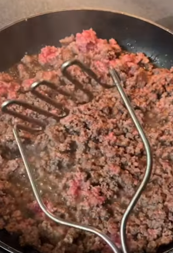 Mashing up ground beef in a skillet with a standard potato masher