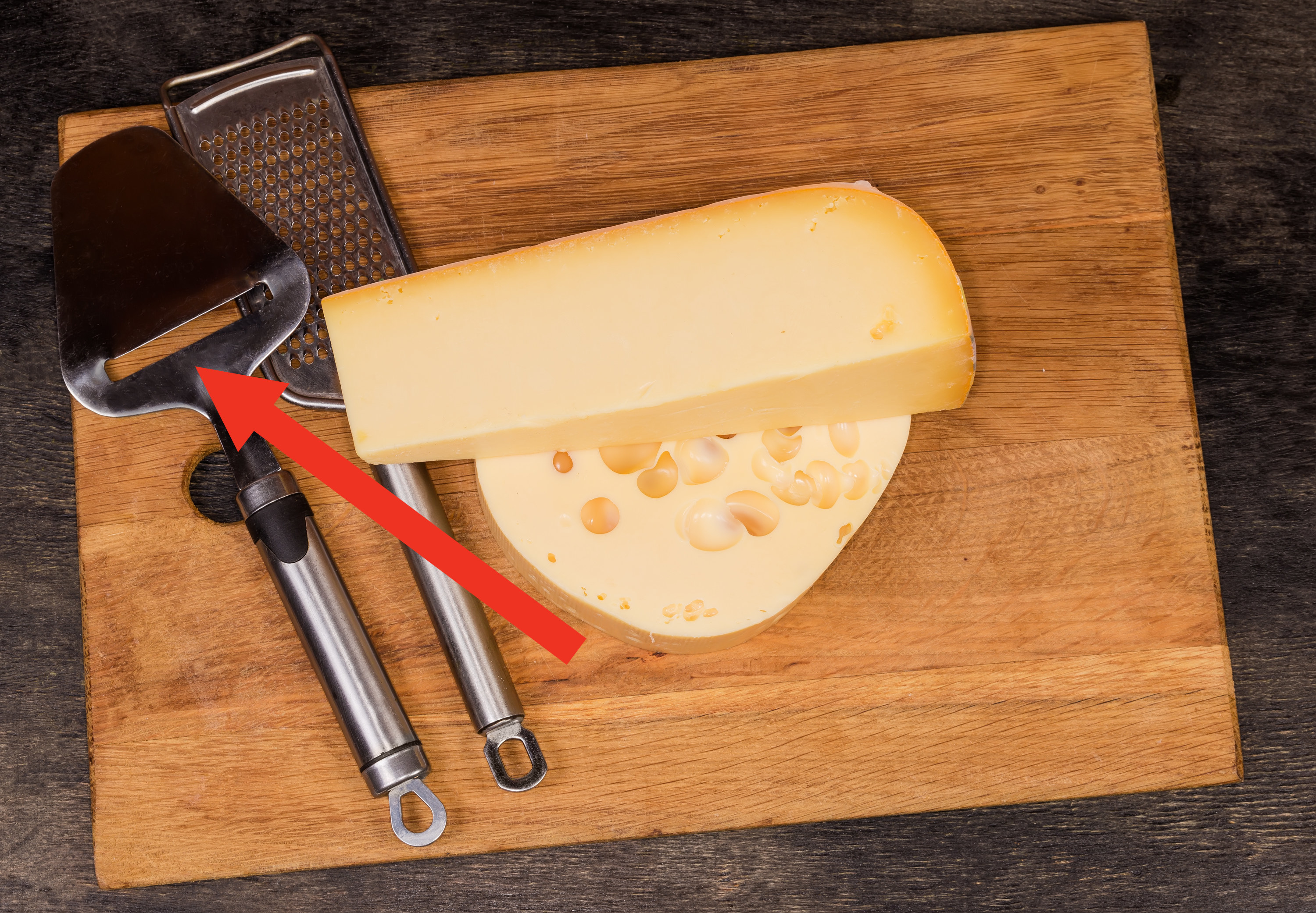 Cheese slicer and grater on a cutting board with two types of hard cheese