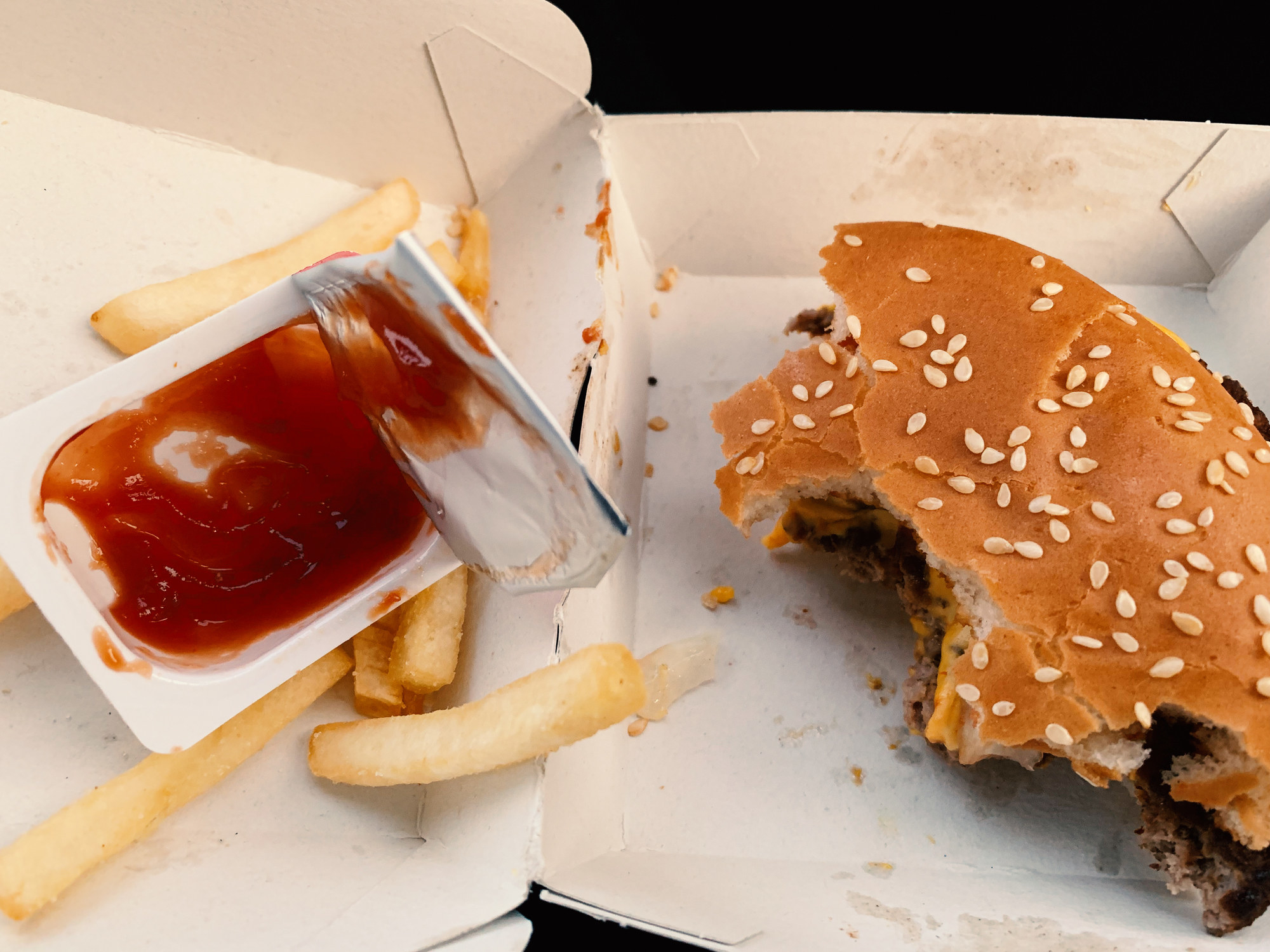 A half-eaten hamburger and fries with ketchup.