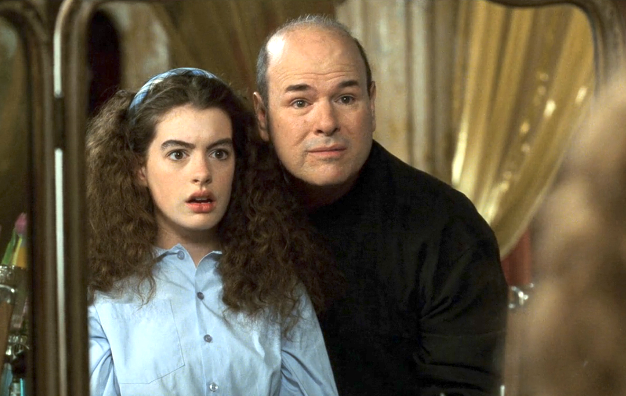 Larry Miller standing by Anne Hathaway and looking in a mirror