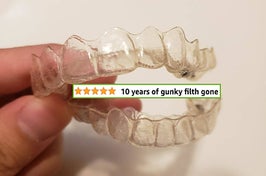 A hand holding a clean mouth aligner with a screenshot of a 5-star review pasted on it that says "10 years of gunky filth gone"