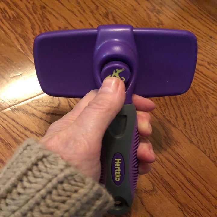 a reviewer photo of a hand holding the purple brush and pushing the clean button