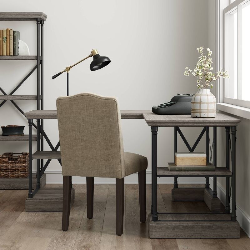 a wood writing desk in gray next to a chair and bookcase