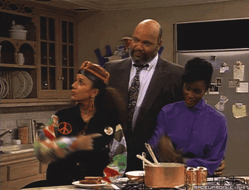 Characters from Fresh Prince of Bel Air raise their fists in air as they stand in the kitchen