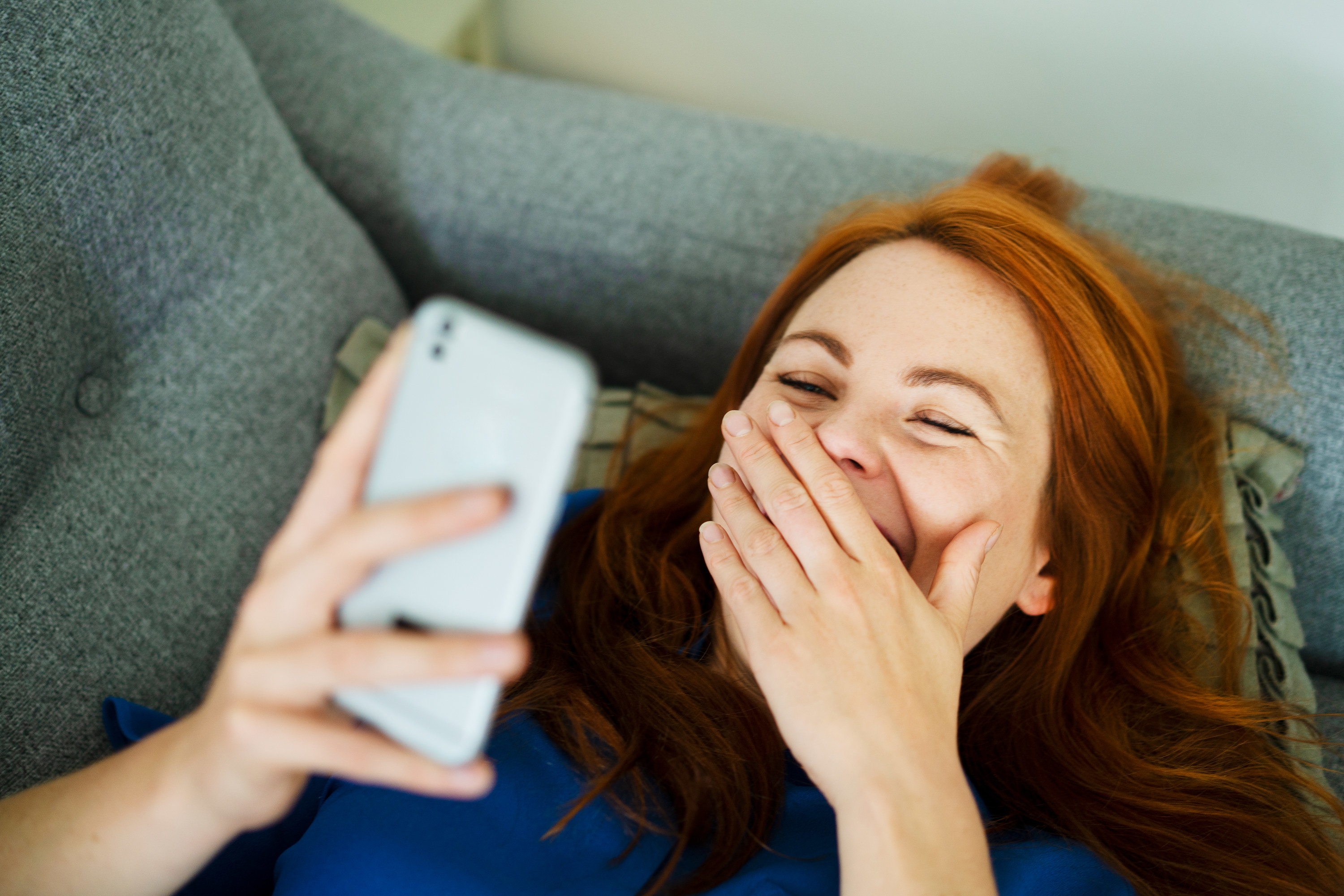 Woman laughs covering her mouth looking at phone