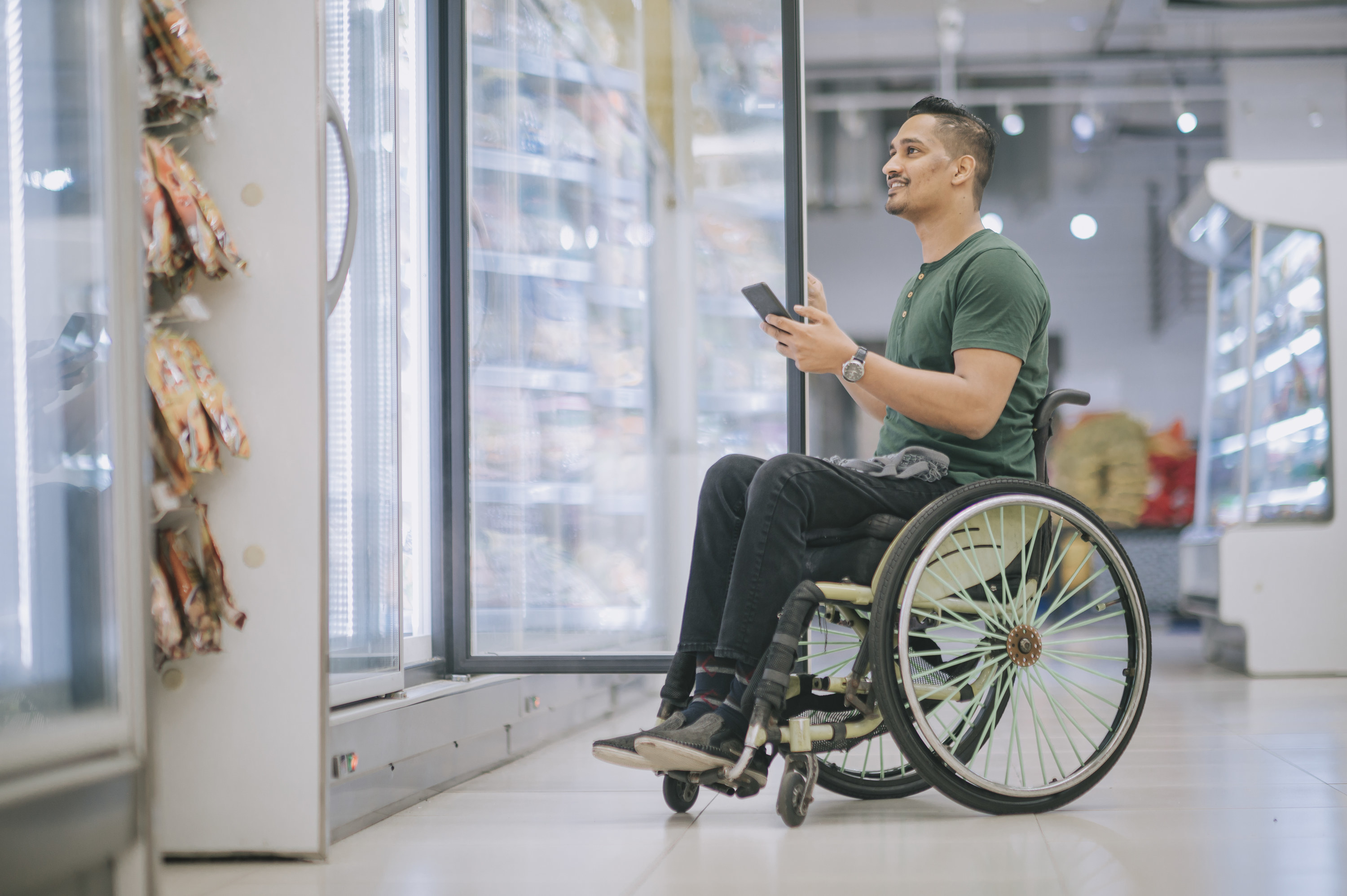 A man in a wheelchair going grocery shopping while he holds his phone