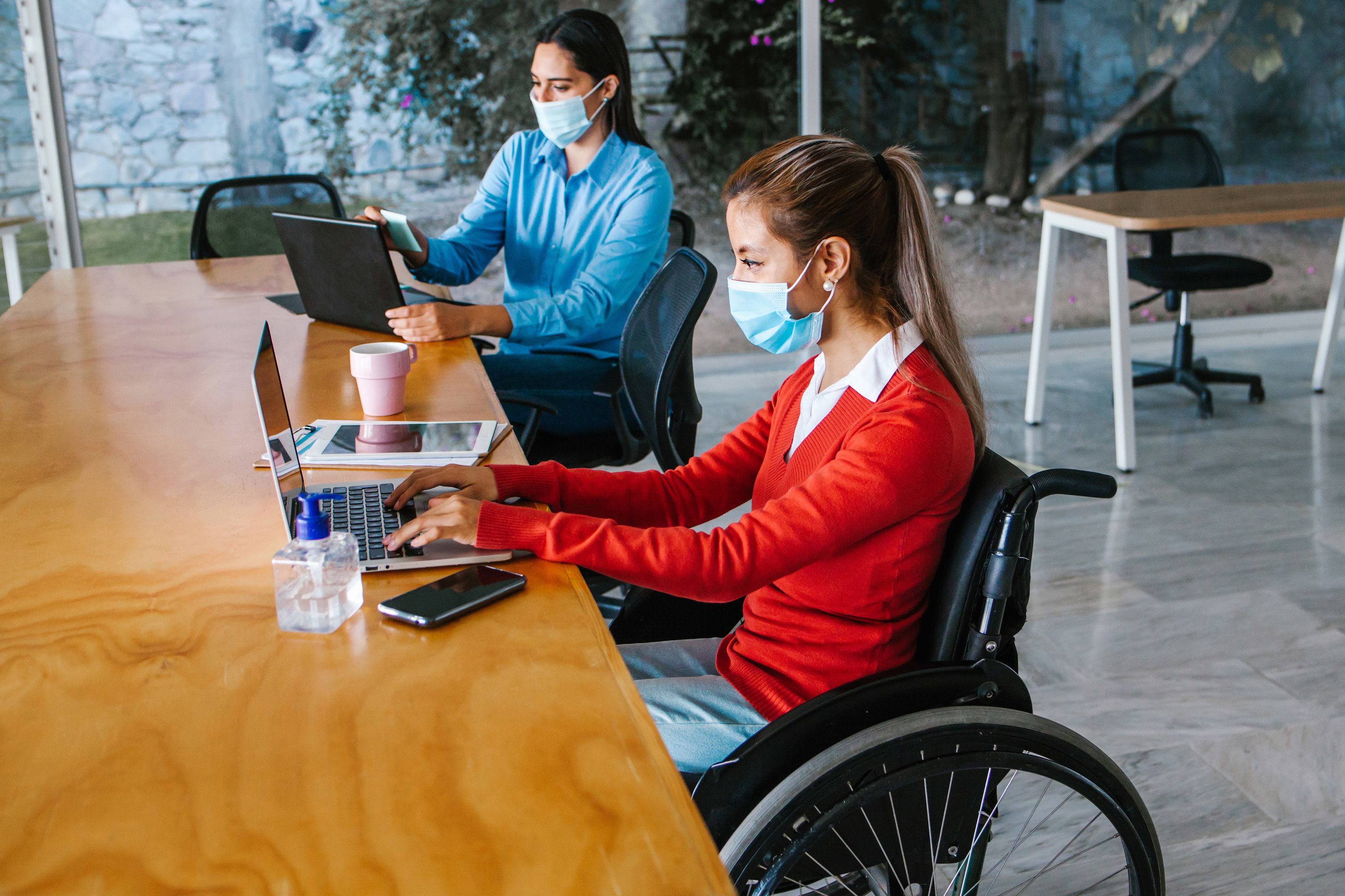 a woman in a wheelchair sitting next to another woman at a table while they work